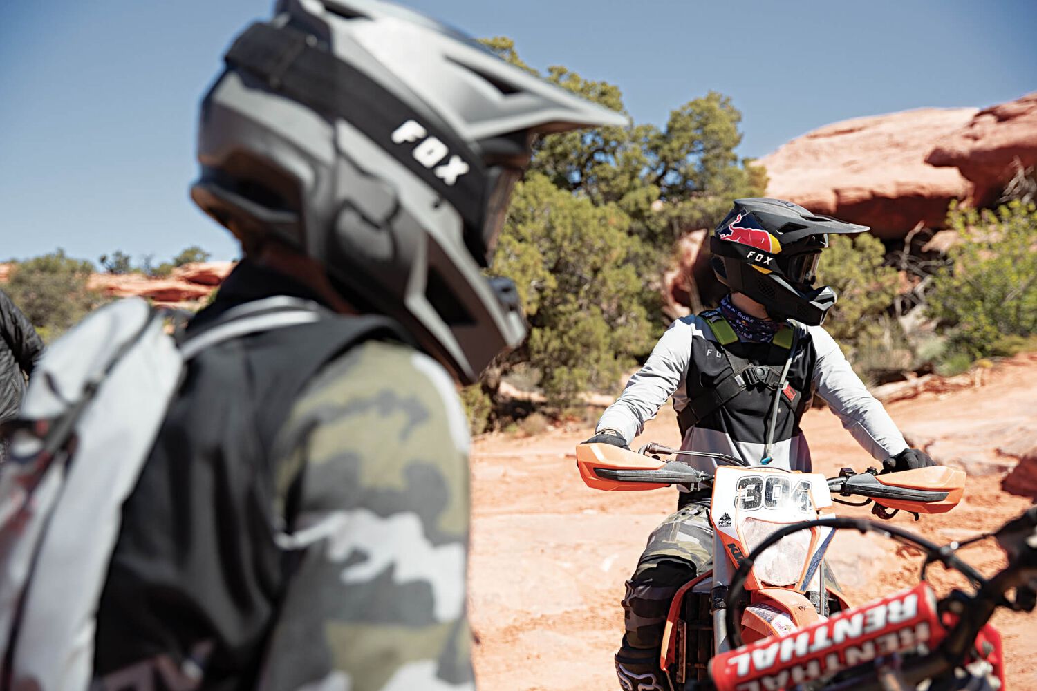 A dirt biker wearing a helmet, camo jersey and hydration pack.